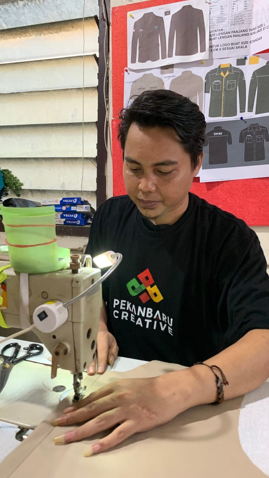 Penjahit Pekanbaru Creative menjahit kemeja di mesin jahit, dengan pola seragam di dinding