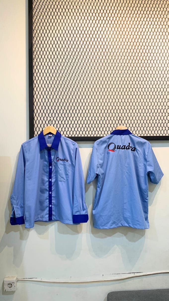 Kemeja kerja biru muda dengan kerah biru tua dan bordir tulisan