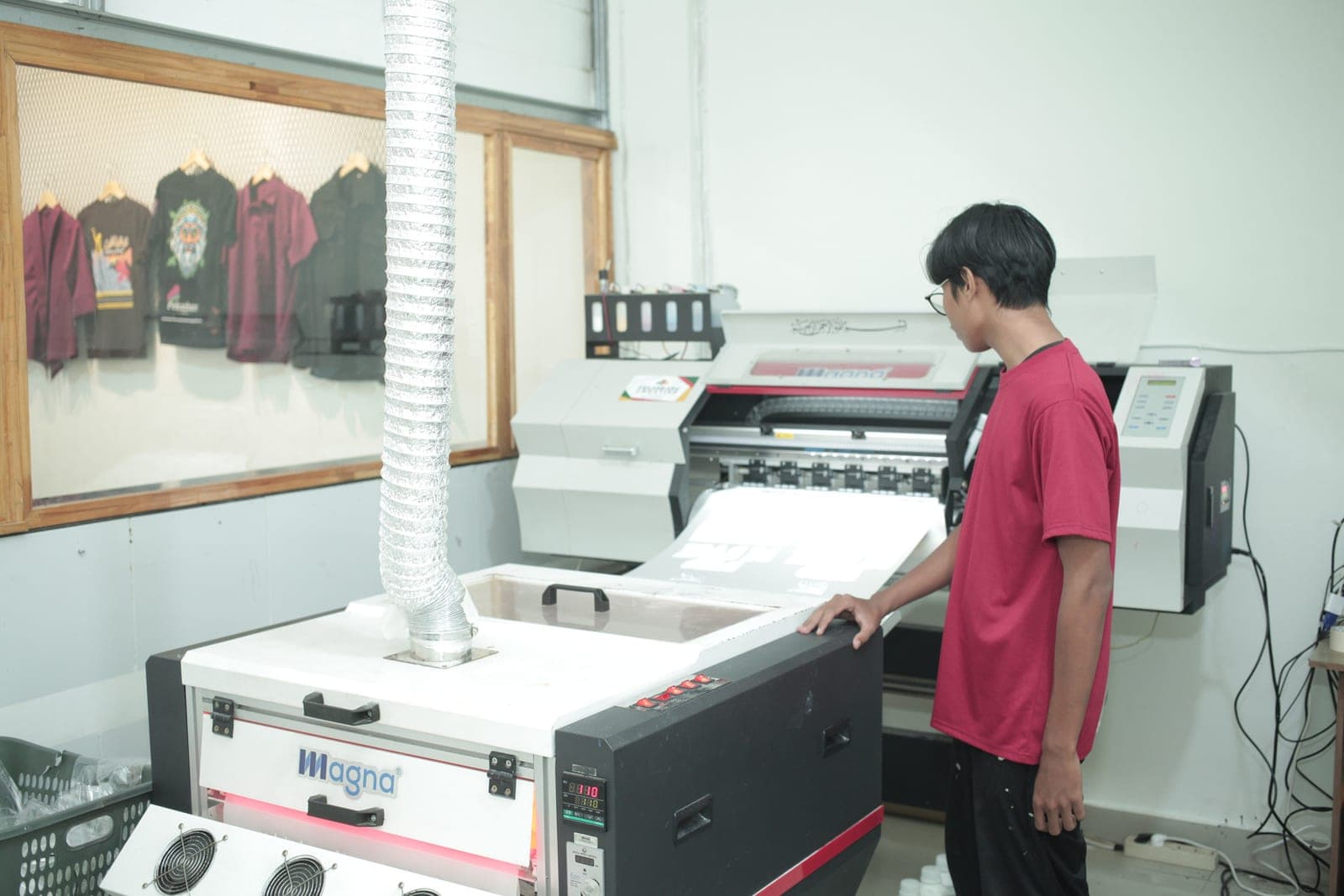Operator di samping mesin cetak DTF dan pengering bubuk di workshop